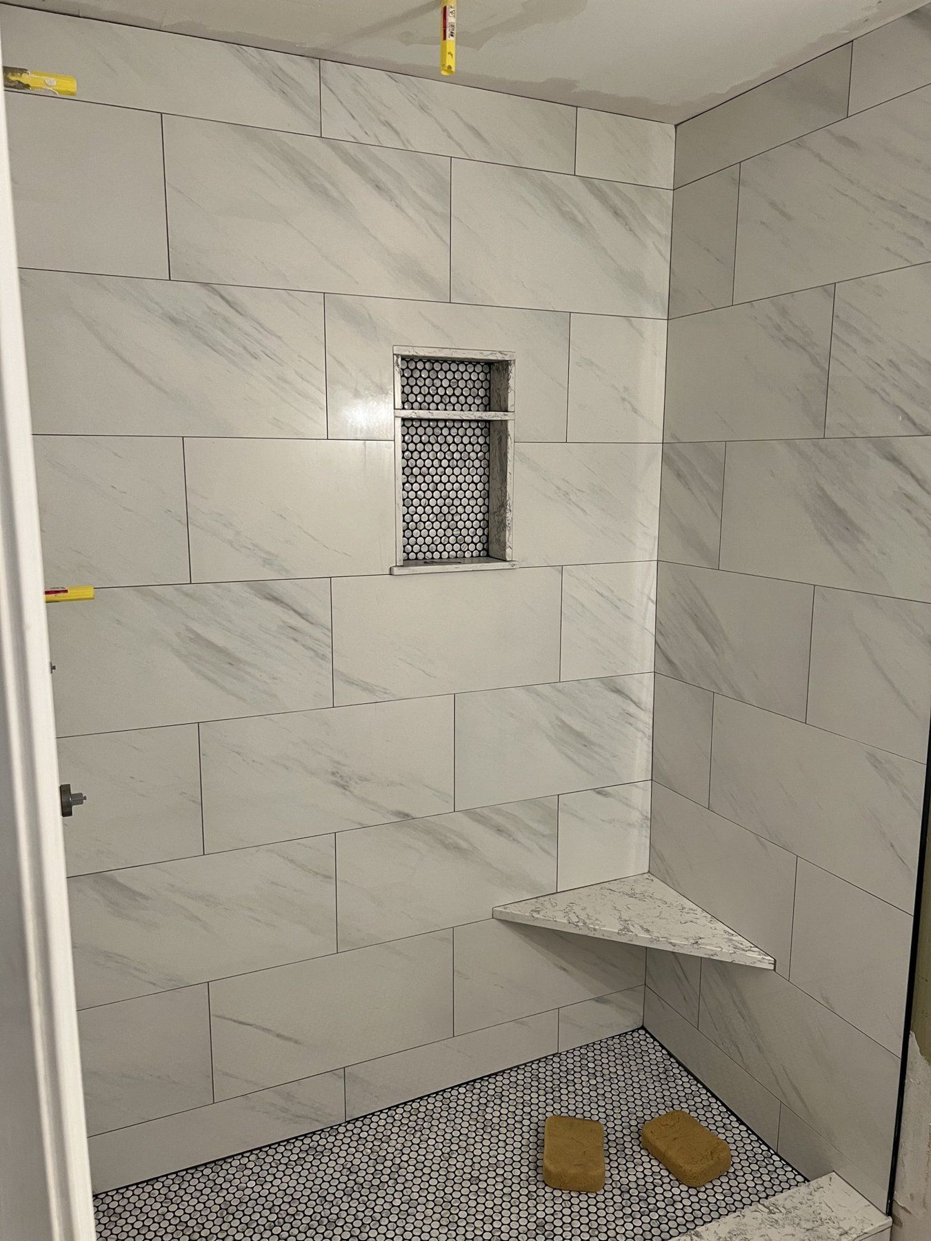 Marble-look tile shower with corner bench and mosaic niche