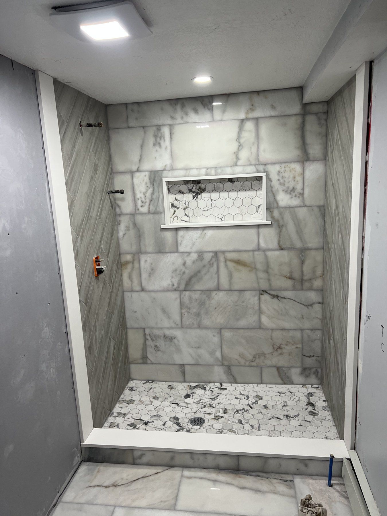 Marble-look porcelain shower with mosaic floor and long niche, tile installation in Massachusetts