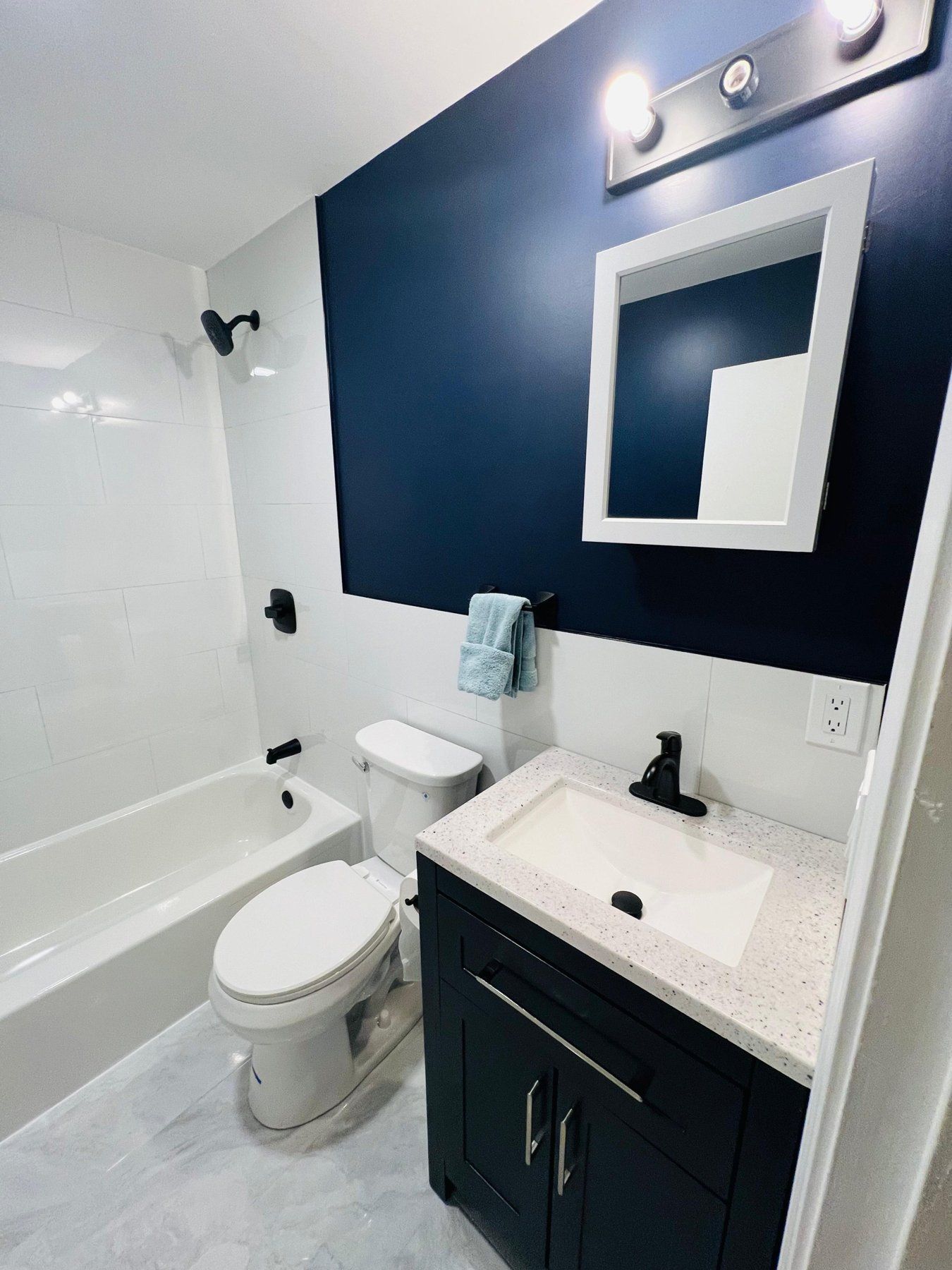 Bathroom with navy accent wall, white tile tub surround and dark vanity