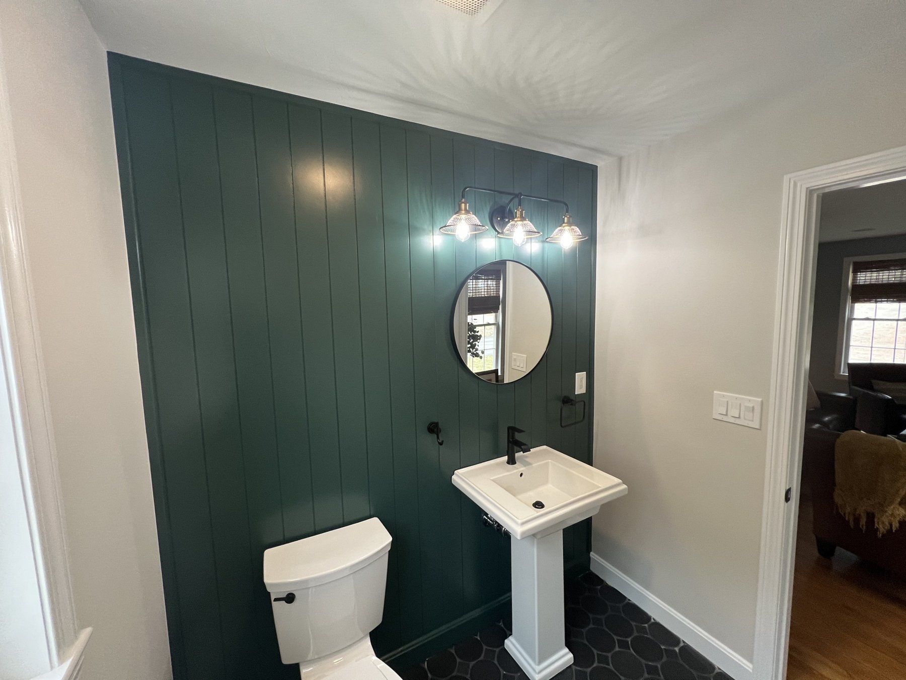 Powder room with pedestal sink, round mirror and green accent wall
