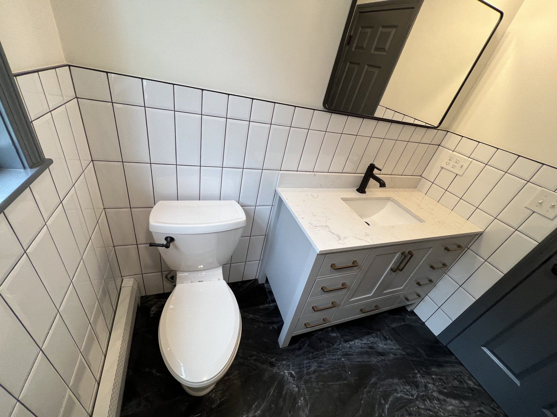 Square white tile wainscot bathroom with dark floor tile