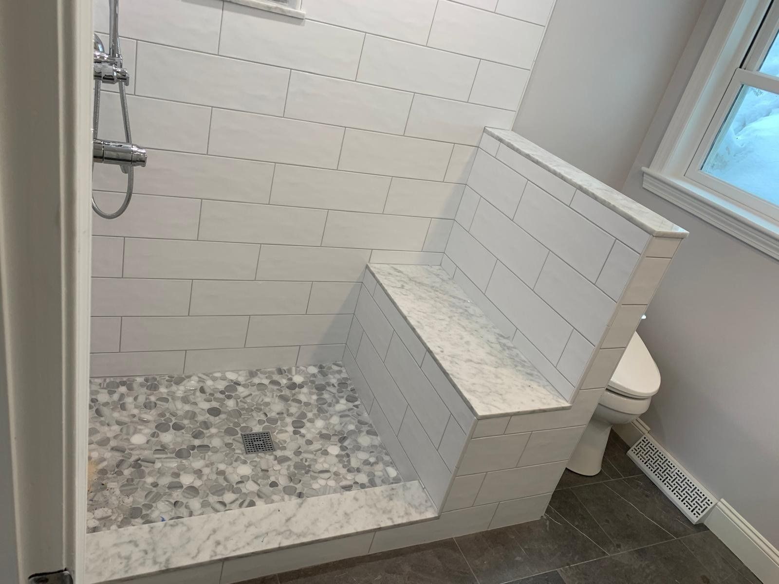 Subway tile shower with built-in bench and pebble floor
