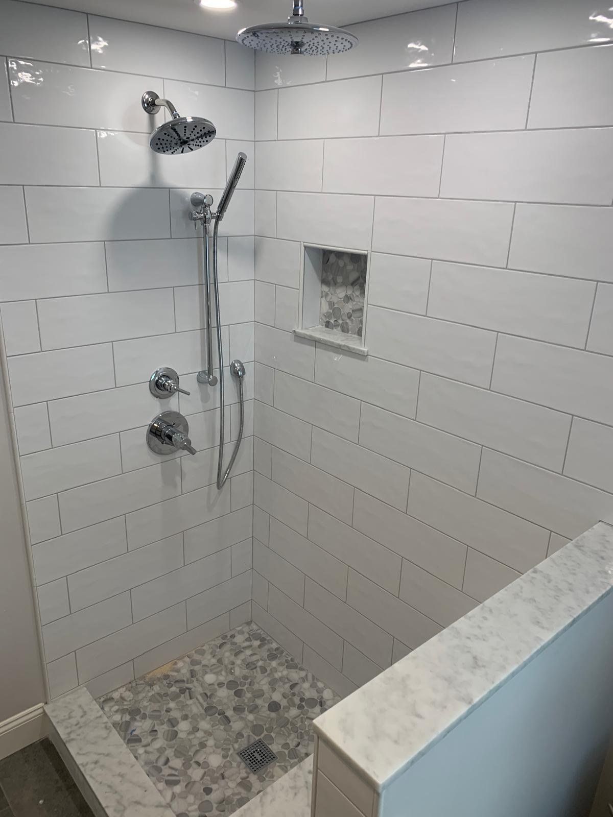 Subway tile walk-in shower with pebble floor and handheld shower