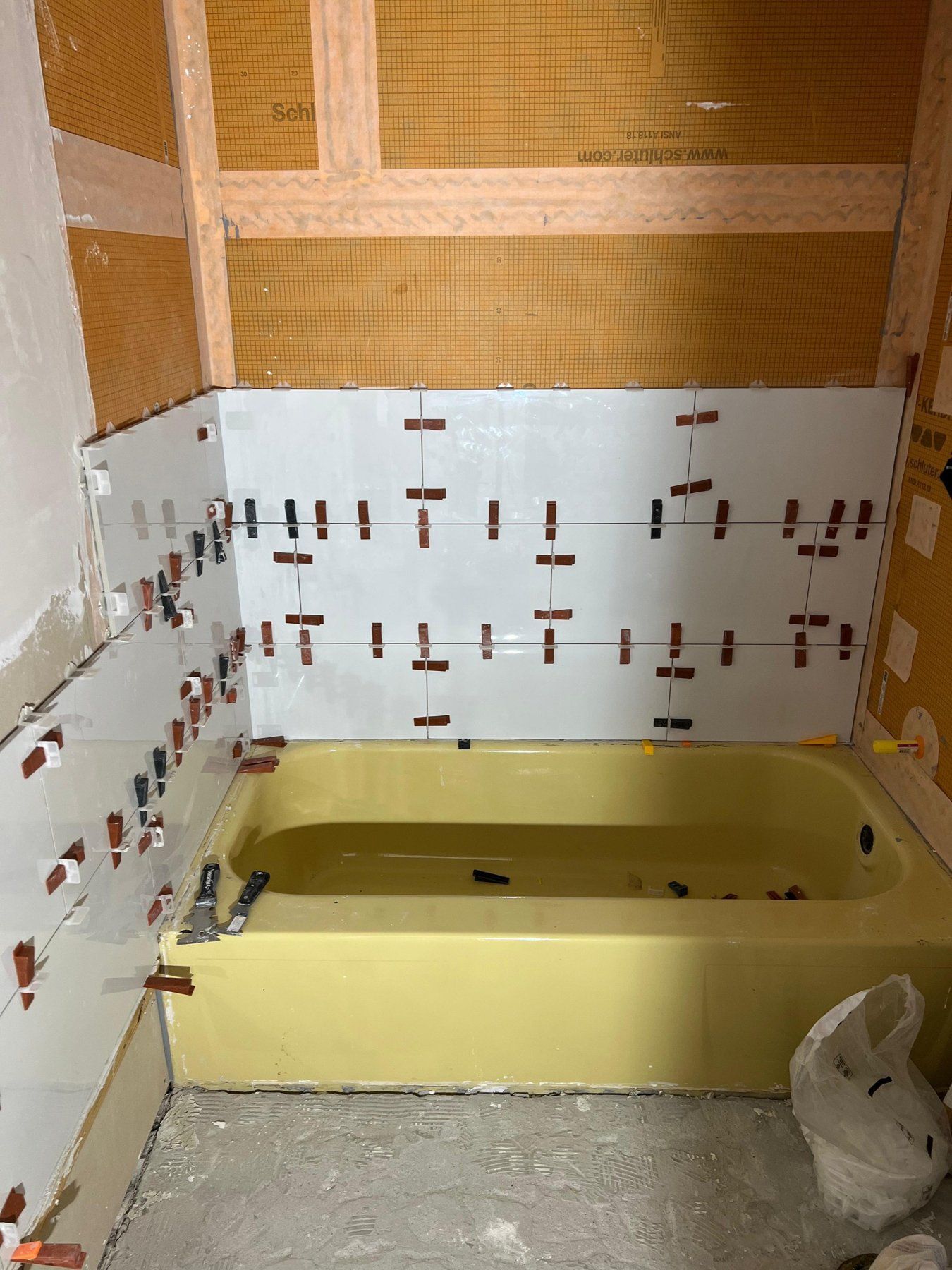 Tub wall tile going up over waterproofing membrane with leveling clips