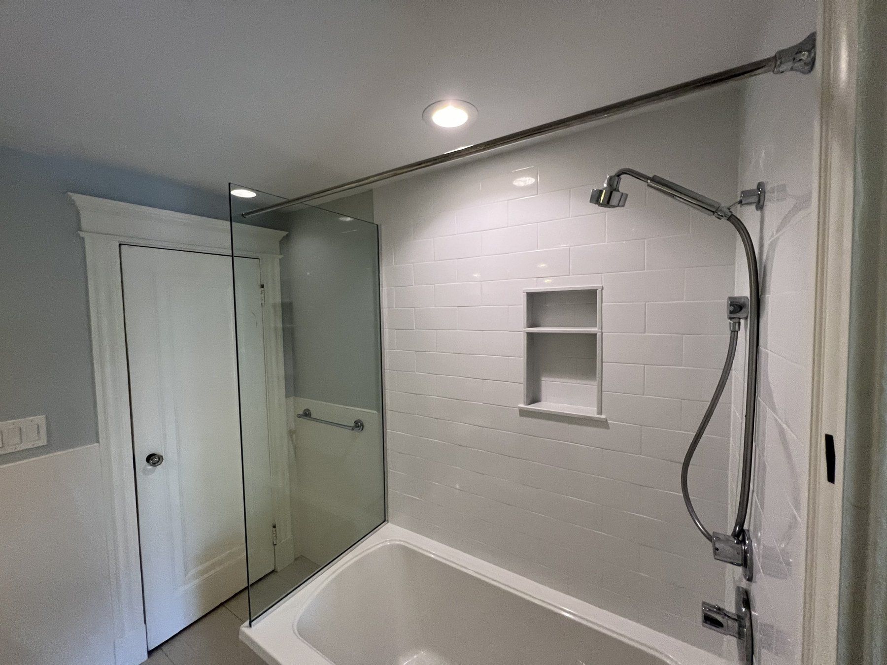 Tub and shower combo with white tile, niche and frameless glass panel, bathroom remodel